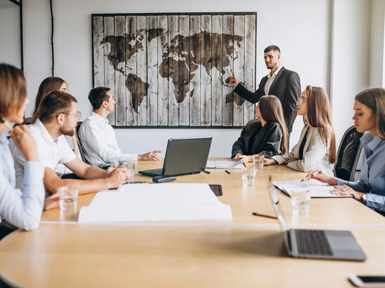 The team around a boardroom table, a world map on the wall behind them